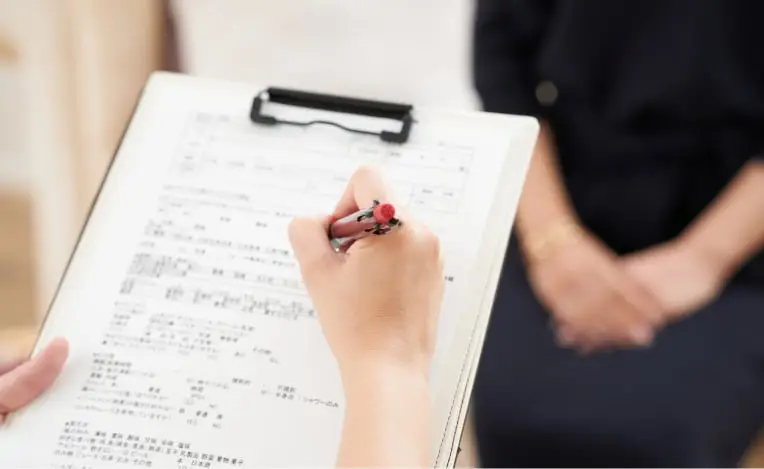 カウンセリング中に問診票を記入する医療従事者の手元と、話を聞く患者の様子